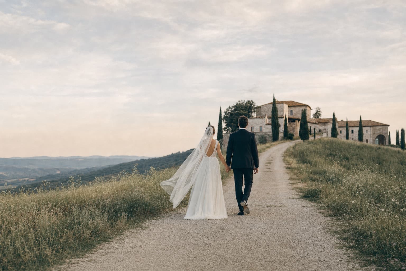 Bride and groom walking hand in hand toward a country estate at dusk — Weddy, the AI wedding planner app for couples