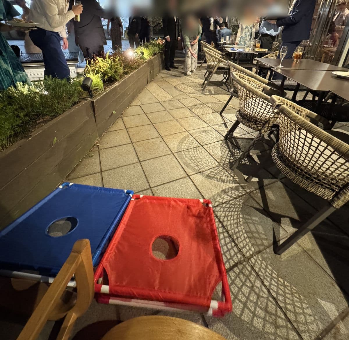 Hochzeitsgäste spielen nachts Cornhole auf der Restaurantterrasse, mit den blauen und roten Cornhole-Brettern im Vordergrund