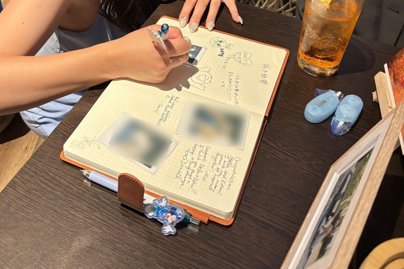 Ein Hochzeitsgast schreibt eine Nachricht in ein aufgeschlagenes Gästebuch, mit Sofortbildfotos auf den Seiten