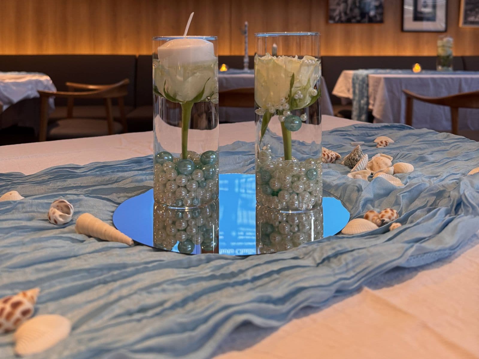 Hochzeitstisch im Meeres-Thema mit Glasvasen mit weißen Rosen, Perlen und schwimmenden Kerzen, sowie Muscheln auf einem blauen Tischläufer